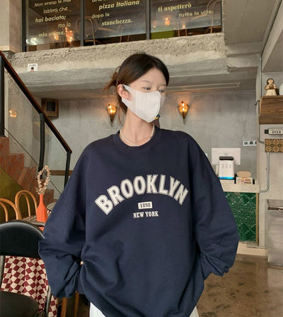 Person wearing a navy blue sweatshirt with 'Brooklyn New York' text in an indoor setting.